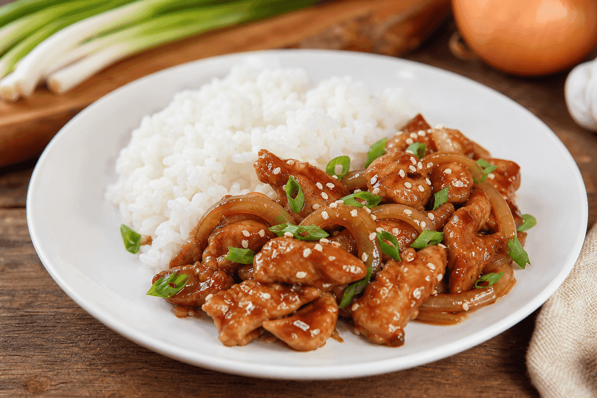 Sepiring ayam teriyaki dengan saus cokelat mengilap, taburan wijen putih dan irisan daun bawang di atas nasi