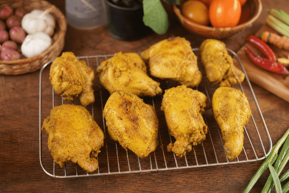 Potongan ayam ungkep bumbu kuning untuk ayam kremes ditiriskan di atas rak kawat sampai permukaannya kering