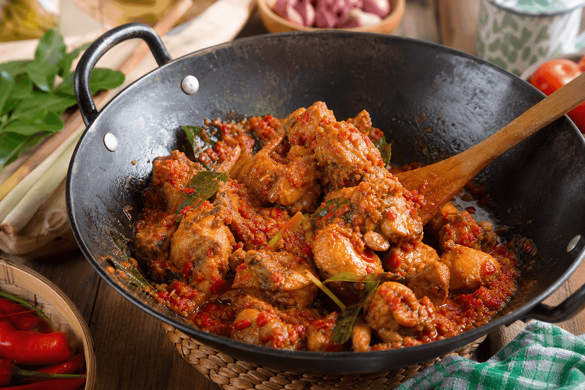 Potongan ayam ditumis bersama bumbu rica-rica merah menyala di wajan besi