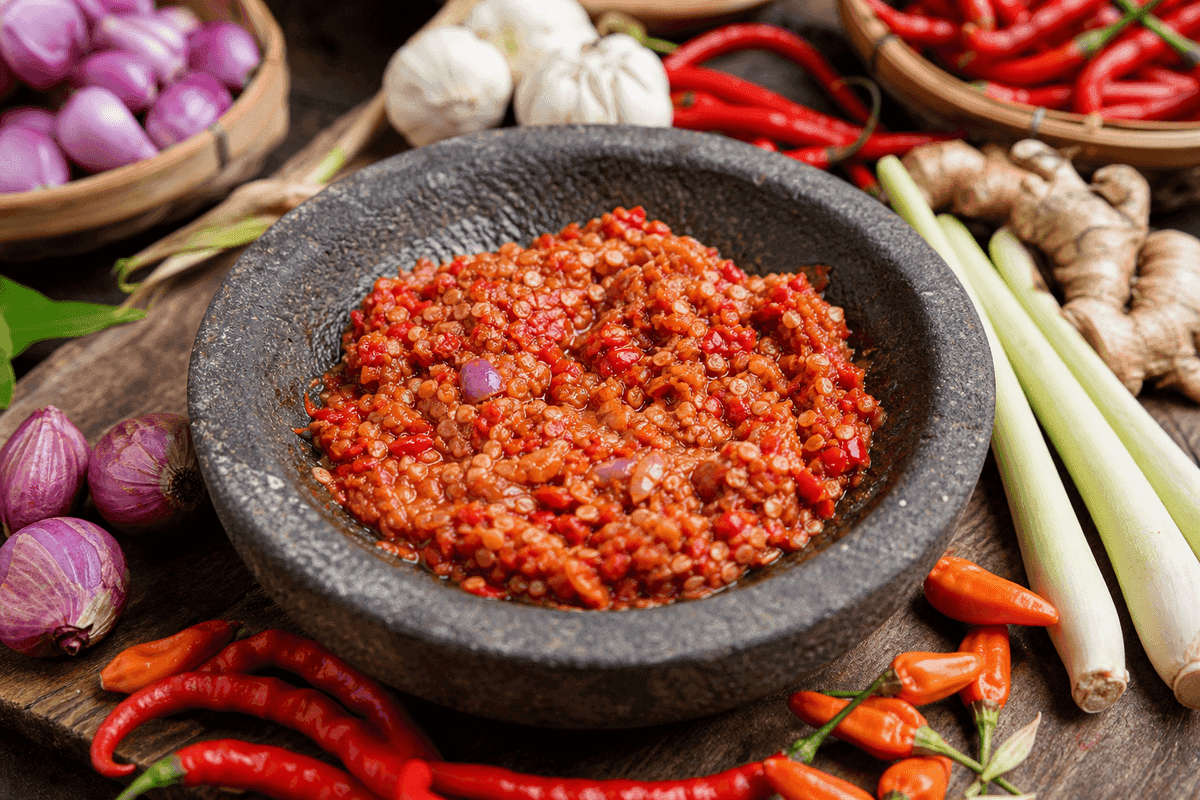 Bumbu rica-rica ayam yang baru diulek kasar di atas cobek batu bersama cabai, bawang merah, dan jahe