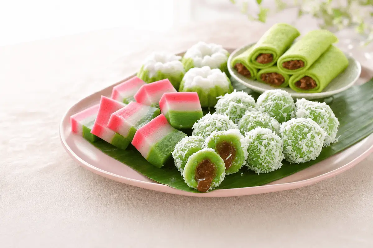 Aneka kue basah tradisional di piring merah muda: klepon berbalut kelapa, kue lapis, putu ayu, dan dadar gulung