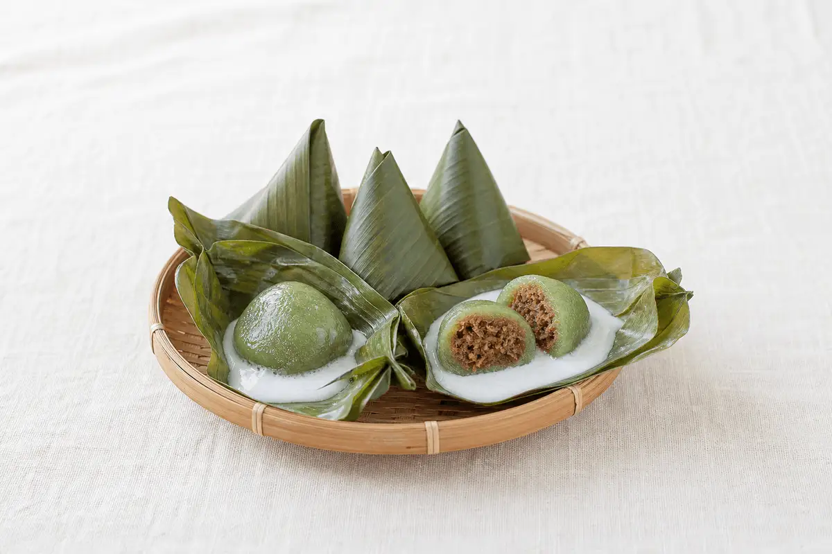 Kue bugis atau mendut bungkus daun pisang, dibuka memperlihatkan kulit ketan pandan, saus santan, dan isi unti kelapa