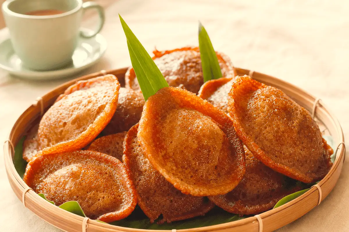 Kue cucur gula merah bertumpuk miring di tampah bambu beralas daun pisang, pinggirannya melengkung dan berkilap minyak