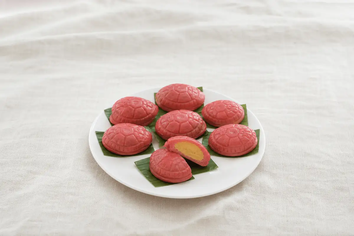 Kue ku merah bermotif tempurung kura-kura di atas potongan daun pisang, satu dibelah memperlihatkan isi kacang hijau