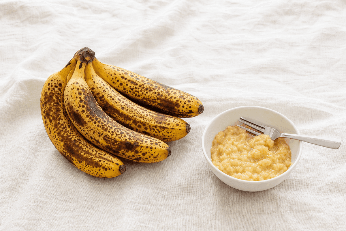 Lima pisang matang berbintik cokelat untuk bolu pisang kukus, di sebelahnya mangkuk kecil berisi pisang yang sudah dihaluskan dengan garpu